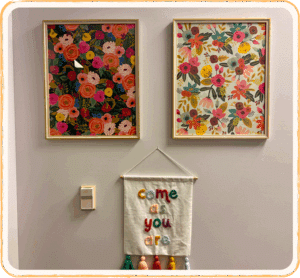 Wall displays two colorful paintings beside a sign reading Come As You Are, conveying acceptance and emotional safety