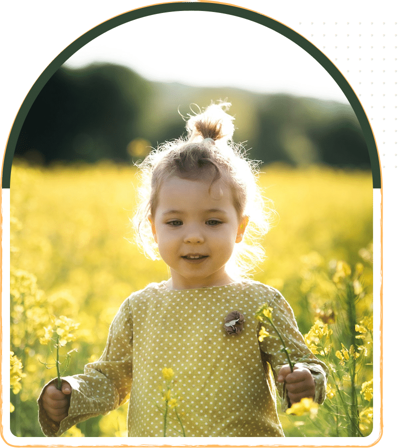 A front view of happy small toddler girl at the field of flowers