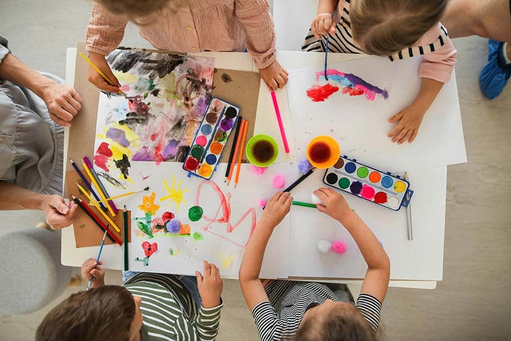 Top view of young children painting with their teacher in a nursery classroom.