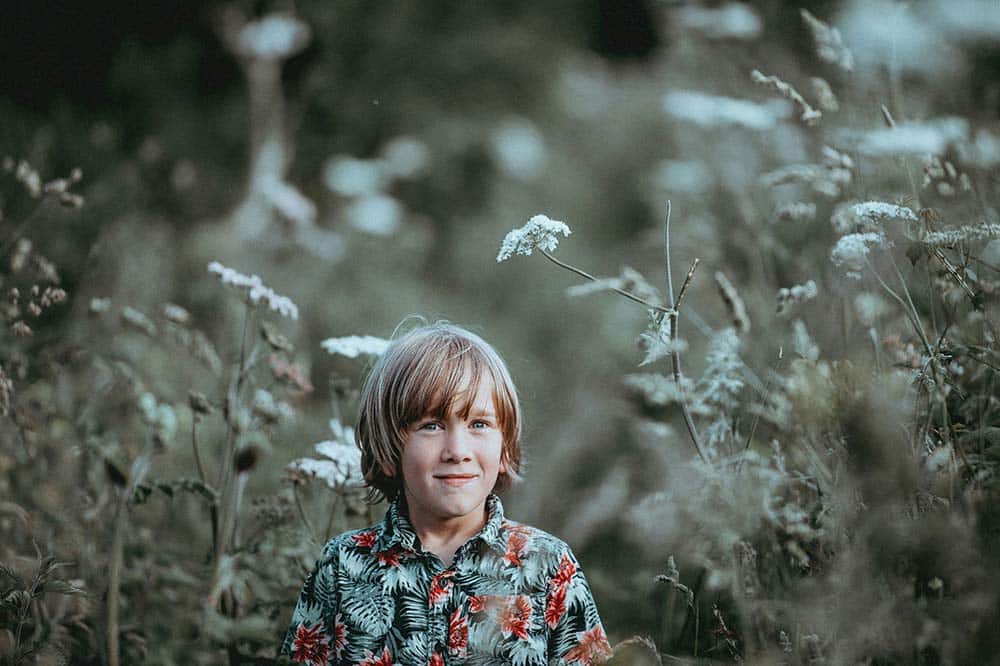 Boy standing among green leafy plants.
